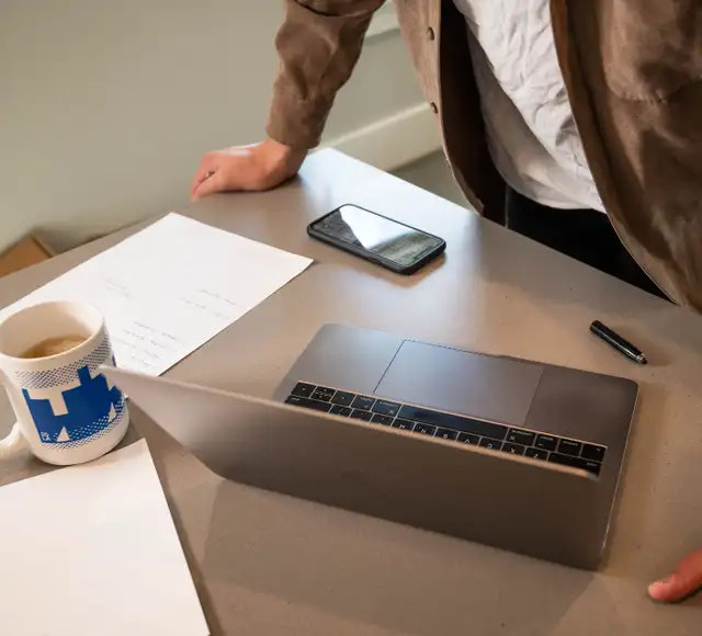 A laptop and papers on a desk being worked through.