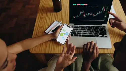 A laptop and a phone on a table, one showing a chart and the other a buy-and-sell screen